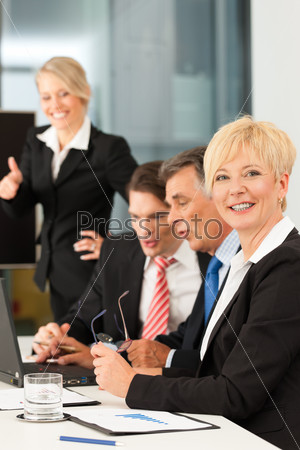 Встреча босса и сотрудников с ноутбуком в офисе. Одна из женщин смотрит в камеру