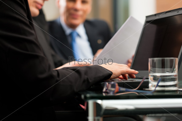 Business - team meeting in an office with laptop, the woman in front is typing
