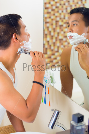 Азиатский мужчина  бреется перед зеркалом