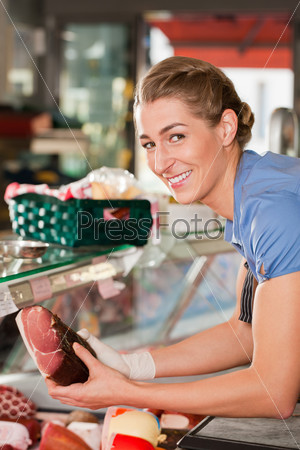 Young woman or female butcher with raw ham in butchers shop, it is probably a shop assistant