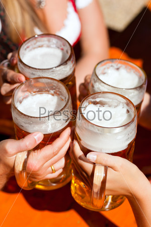 Four friends with a fresh beer in a Beer garden, close-up on beer stein