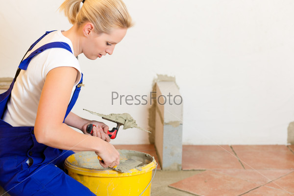 Female construction worker is tiling at home; she is presumably a do-it-yourself