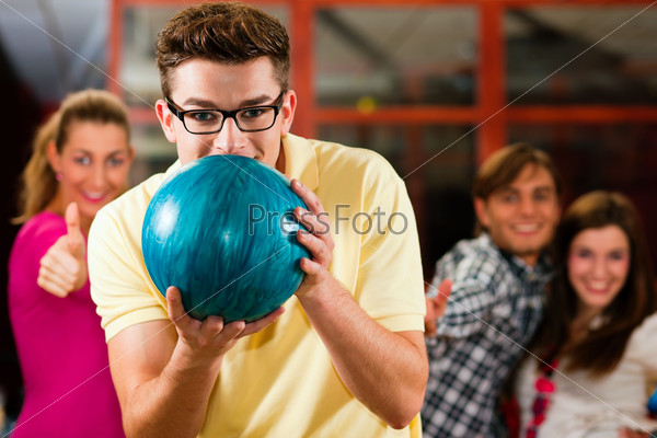 Group of four friends in a bowling alley having fun, three of them cheering the one in charge to throw the bowling ball