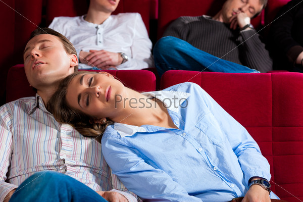Couple and other people, probably friends, in cinema watching a movie, it seems to be a boring movie, stock photo