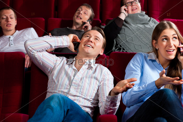 Couple and other people, probably friends, in cinema watching a movie, everybody is making a phone call, it seems to be a boring movie