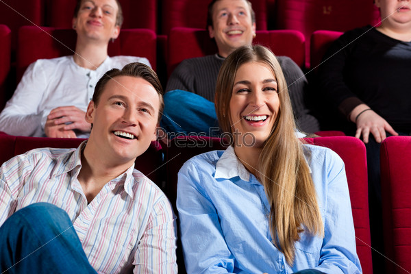 Couple and other people, probably friends, in cinema watching a movie; it seems to be a funny movie