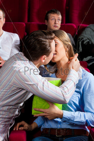 Couple in cinema watching a movie, they eating popcorn and kissing