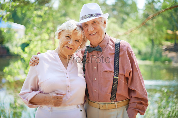 Happy seniors in smart casual looking at camera in park, stock photo