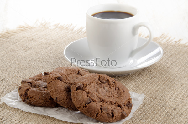 Chocolate biscuit on white paper and a cup of coffee in the background, stock photo