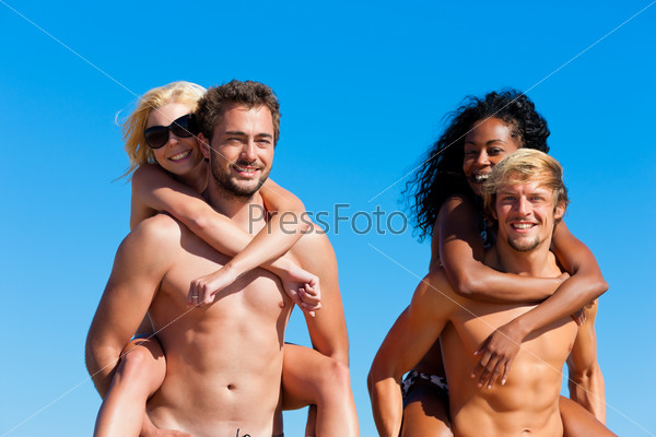 Four friends - men and women - on the beach having lots of fun, the men carrying the women pack back
