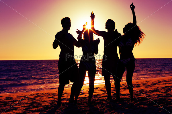 People (two couples) on the beach having a party, drinking and having a lot of fun in the sunset (only silhouette of people to be seen, people having bottles in hands with the sun shining through)