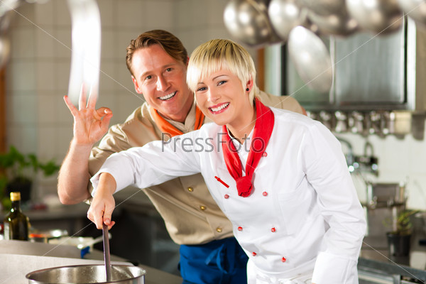 Two chefs in teamwork - man and woman - in a restaurant or hotel kitchen cooking delicious food