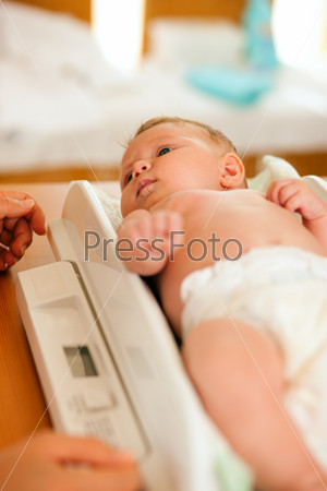 Baby on a weight scale, her mother or a doctor is checking health and development of the newborn