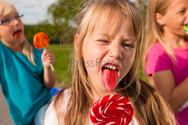 Three girls eating lollipops, the girl in front sticking her tongue out