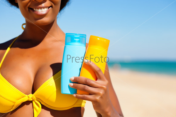 Woman in yellow bikini offering suncream on the beach in order to avoid sunburn, FOCUS is on hand, lots of copyspace