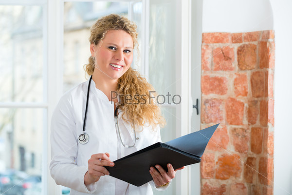 Young female doctor sitting on a desk in front of window in clinic with test results in a file or dossier