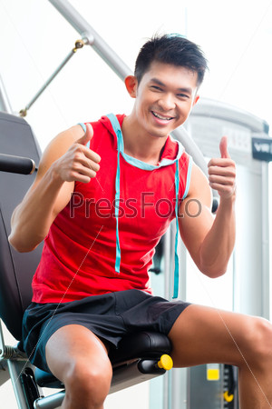Asian Chinese man having fitness training or workout in gym doing sport to build up muscle on a weight machine