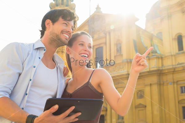 Man and woman or young couple making trip as tourists in Munich at the Odeon Church with city map on the tablet computer for navigation