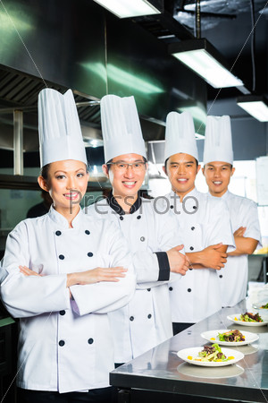 Asian Indonesian and Chinese chefs along with other cooks in restaurant or hotel commercial kitchen cooking, finishing dish or plate