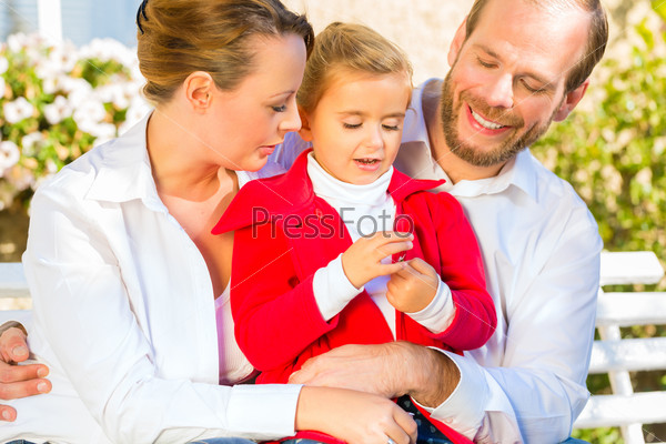 Family with mother, father and daughter together on garden bench in front of home
