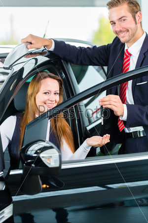 Seller or car salesman and female client or customer in car dealership presenting the interior decoration of new and used cars in the showroom and hands over the car keys