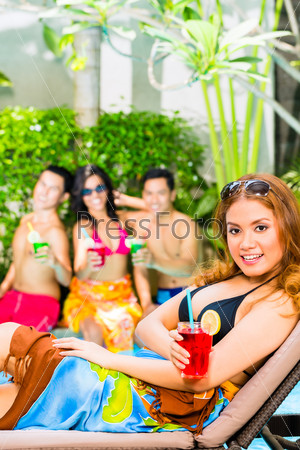 Asian friends partying and drinking fancy cocktails at hotel or club pool party, stock photo