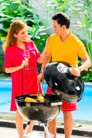 Asian handsome couple drinking wine and having barbecue party or BBQ outside at the pool with grilled corn cobs