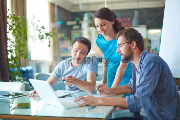 Group of three successful business partners in casual discussing data in laptop at meeting in office, stock photo