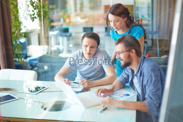 Group of three successful business partners in casual using laptop at meeting in office