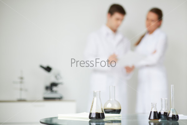 Test-tubes with liquid oil on background of two scientists working in laboratory