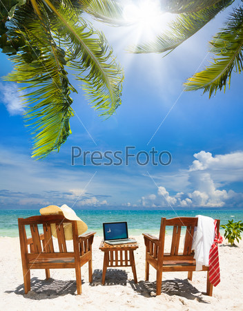 Chairs, laptop and put away tie and white collar shirt, straw hat. Chairs and table on the beach on sunny day