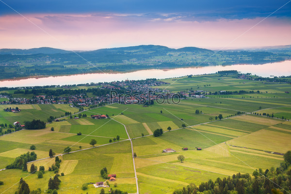Areal photograph of read crossing, green fields stripes, trees and houses near Neuschwanstein castle in Germany