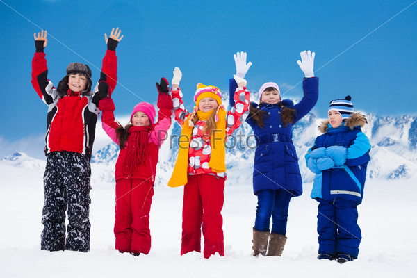 Group of five super happy kids standing in snow with lifted hands
