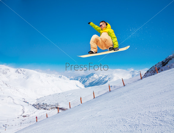 Cute handsome snowboarder man holding snowboard in the air jumping in ski park