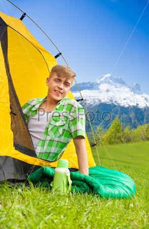 Beautiful young man with red hair in a tent smiling, on her hiking trip