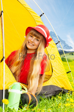 Portrait of blond happy smiling little years old girl sitting in camping tent in yellow dandelion field