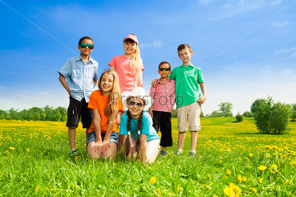 Group of happy diversity looking kids, boys and girls standing in the spring dandelion field
