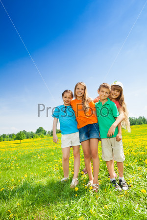 Four happy smiling boys and girls standing together in the flower field