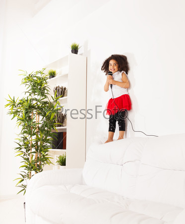 Cute little black African three years old girl with cute curly black hair with microphone performing standing on the coach
