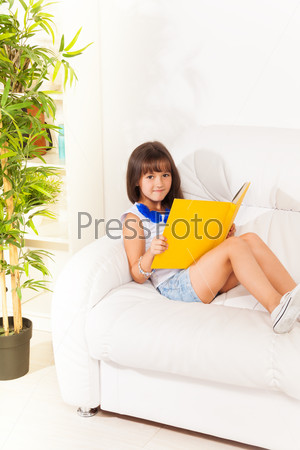 Nice brunet girl sitting and reading book on the sofa at home