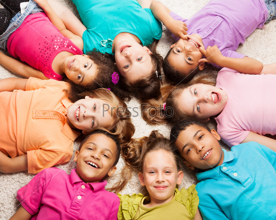 Group of eight happy diversity looking kids, boys and girls laying in star shape on the floor