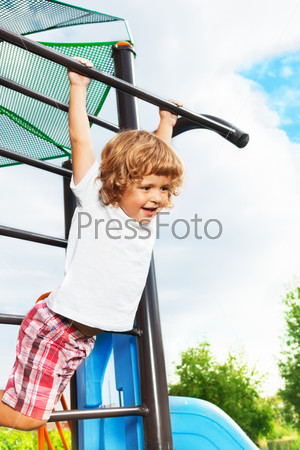 Happy three years old boy about to hand on the horizontal bar on playground
