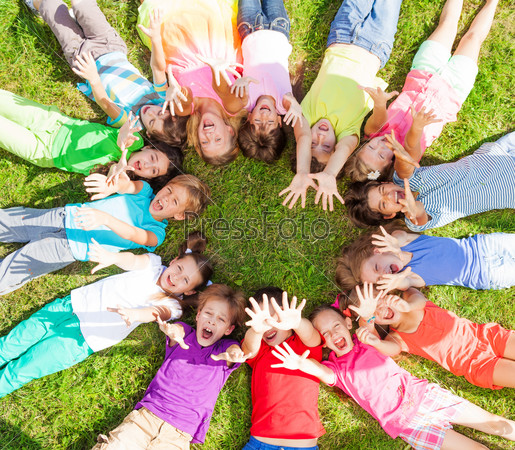 14 Kids Laying In A Circle In The Grass With Happy Faces Shoot From Above Lifting Hands Above