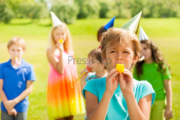 Handsome boy blowing twisted whistle in party horn with many kids on the background