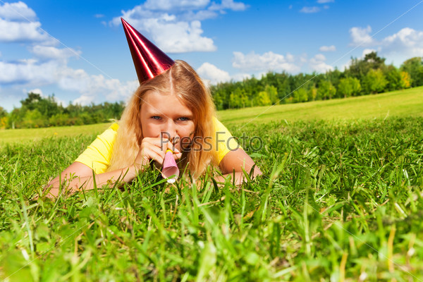 Beautiful teen girl with noisemaker horn and birthday party cap laying outside with happy expression on sunny summer day