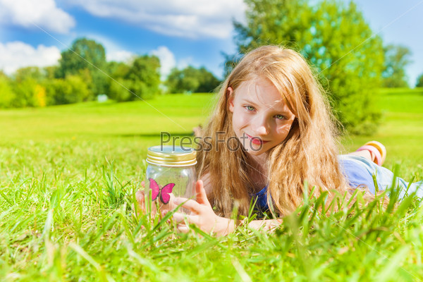 Portrait of happy smiling girl with long dark hair 8 years laying in the grass old hold jar with butterfly standing in the park on bright sunny summer day