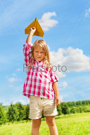 Beautiful little girl throwing yellow paper plane on bright sunny summer day in the park