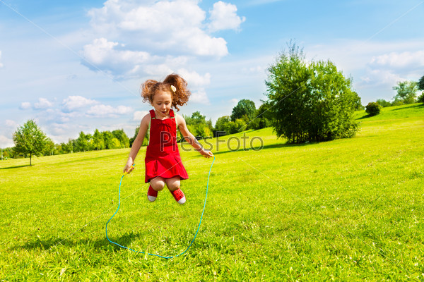 Beautiful little 6 years old girl jumping over the rope in the park on sunny summer day
