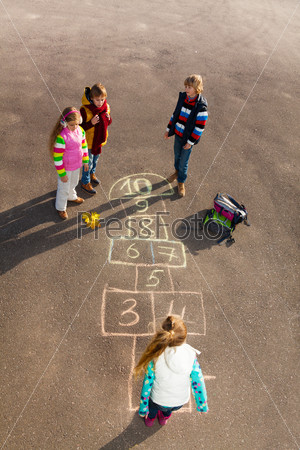Group of kids jumping on the Hopscotch game drawn on the asphalt after school wearing autumn clothes