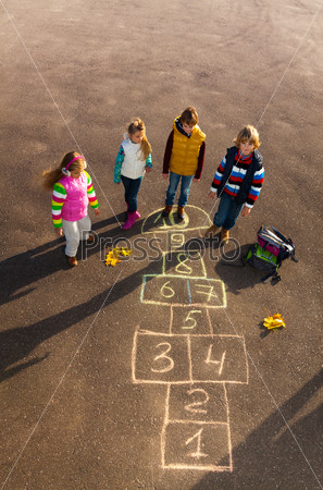 Group of kids jumping on the Hopscotch game drawn on the asphalt after school wearing autumn clothes after school